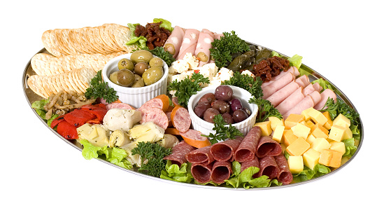 An antipasto catering platter of continental meats and feta cheese over a bed of mixed greens plus marinated artichoke hearts, olives, sun dried tomatoes and marinated eggplant. Served with crackers on a silver platter.