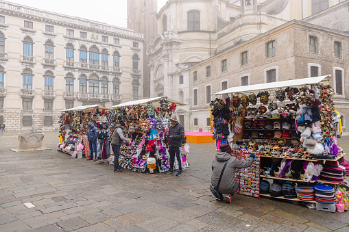 Venice, Italy - February 16 2023: Stone paved square with market stalls in Venice, selling masks and other souvenirs at the time of Carnival on a foggy day at wintertime