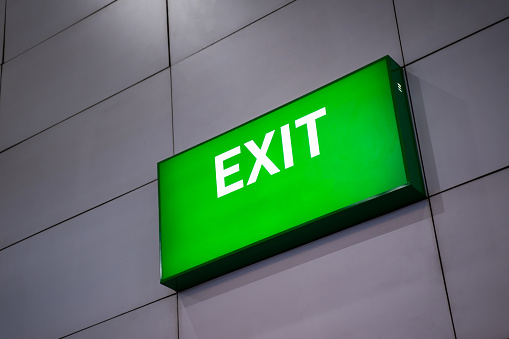 A green fire escape sign is stuck on the ceiling. Green exit sign at the exit door.