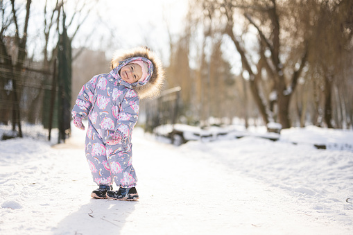 Baby girl wear child snowsuit on a sunny frosty winter day.