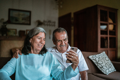 Senior couple using a mobile phone sitting on sofa in the living room at home