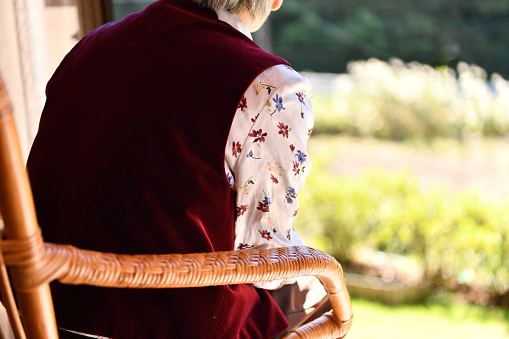 Japanese senior woman sitting on a rattan chair by the window