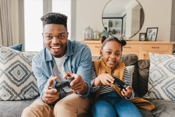 istock Front view of young father and daughter playing video game on sofa 1792968041