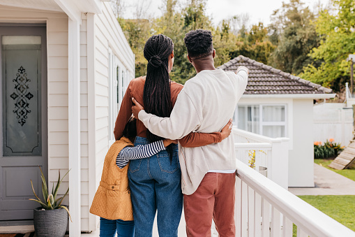 Couple with daughter  hugging each other, standing on terrace of new home, pointing and looking into distance