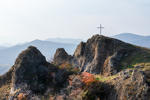 rock with a cross on top in the mountains of Georgia against the blue sky