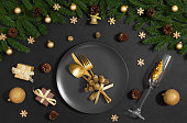 Black table setting with golden Christmas decorations and cutlery. New Year's eve serving on black background. Christmas dinner. Top view, flat lay.