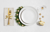 Christmas table setting with golden decorations and empty beige plate on white background. New Year serving with empty plate for design. Top view, flat lay.