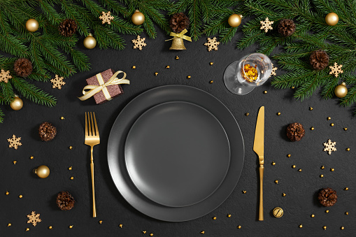 Christmas table setting with black empty plate, gold cutlery and festive decor on a black background. Preparing for Christmas dinner. Happy new year. Top view, flat lay.