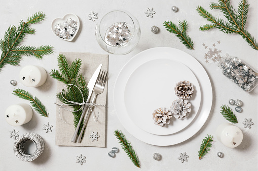 Festive table setting for Christmas dinner on a white background. New Year serving with silver decor, fir branches and cones. View from above.