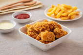 Crispy popcorn chicken in bowl with french fries on plate and sauce