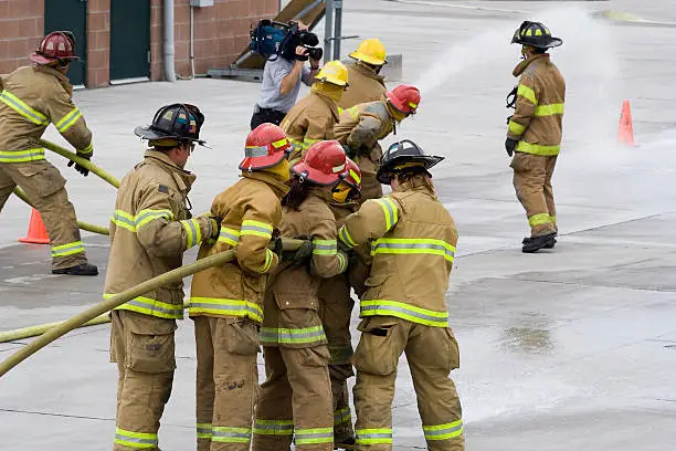 Firefighters in training, learning to handle the firehose. Notice the cameraman in the background.