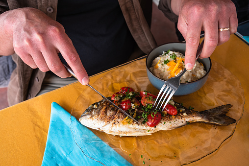 Man eating grilled bream fish and rice with celery root puree in a seaside Provencal restaurant in Camargue, France. Simple healthy delicious local food. Food background. Foodie lifestyle concept.
