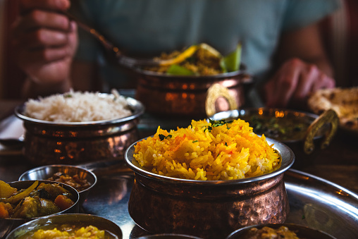 Man (unrecognizable) eating traditional food in an Indian restaurant. Vegetarian Thali set on the tray, chicken curry, rice, naan and other delicious dishes on the table. Foodie travel background.