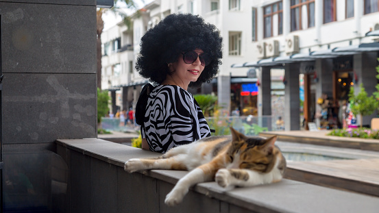 A girl with curly black hair with cat in city center. Friendship between man and animal.
