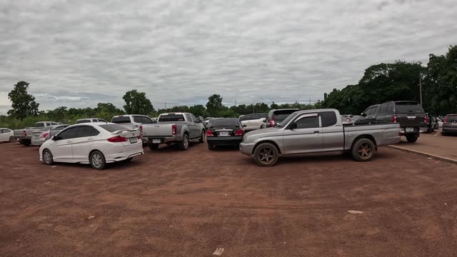 A wide, close-up view of walking past a multitude of cars parked completely on the red dirt parking lot.