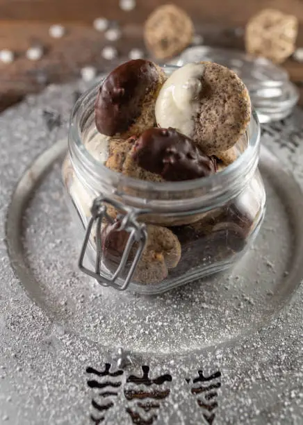 Delicious poppy seeds cookies for christmas season in a glass jar on a silver plate on wooden table background.