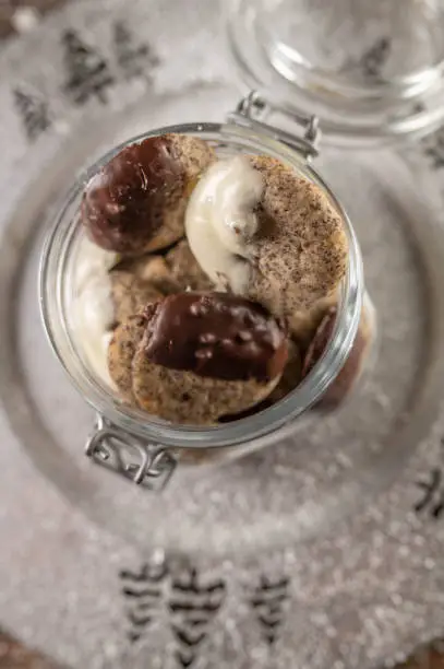 Delicious poppy seeds cookies for christmas season in a glass jar on a silver plate on wooden table background.