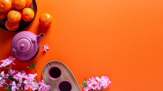 Chinese or lunar new year flat lay with mandarins, pink peach flower and tea set on orange background, top view, web banner