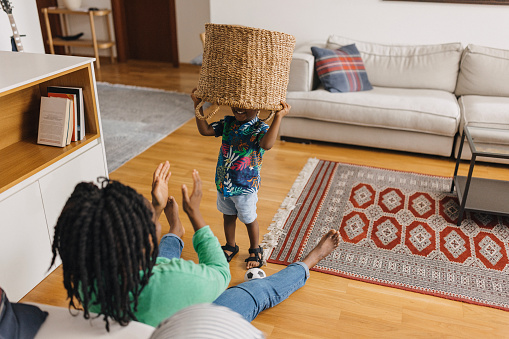 Mother and son playing with a wooden basket. The kid is putting basket on his head