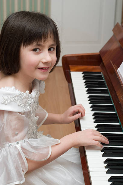 girl playing piano Young girl in white dress playing piano girl playing piano stock pictures, royalty-free photos & images