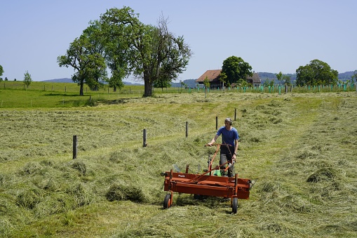 Wetzikon, Switzerland – May 28, 2023: A rugged male farmer harvesting hay with a small tractor