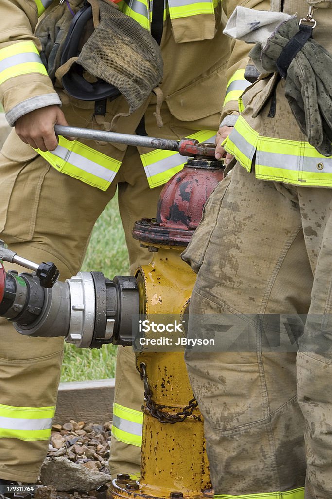 Opening a Fire Hydrant Firefighters work to open a fire hydrant in order to attach their fire hose. Accidents and Disasters Stock Photo