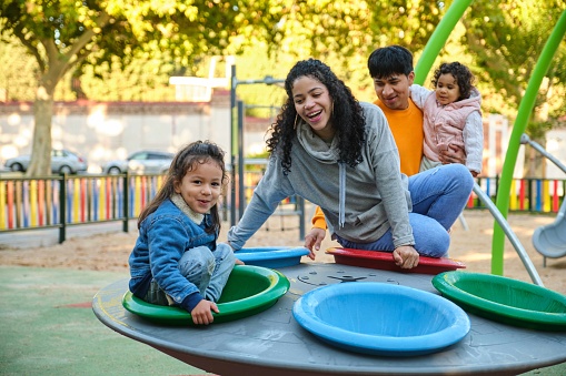 Latin family with two children playing together in a playground. Hispanic family.