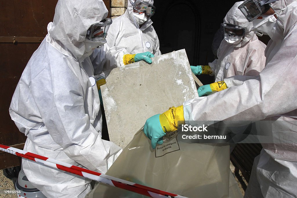 Removing materials containing some asbestos "Staff removing some asbestos in a post of transformer, Reflection of mask of man opposite was created for cannot be recognized" Asbestos Stock Photo