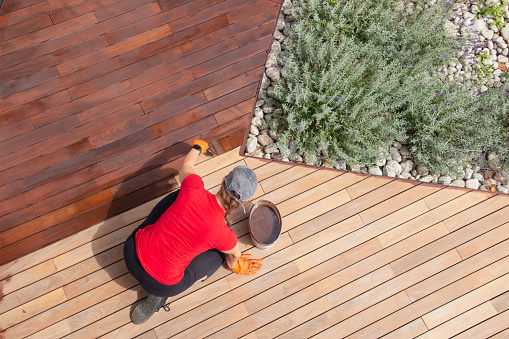 Refreshing of wood deck boards with UV protection pigment oil. Female staining wooden floor terrace in exterior backyard of the house