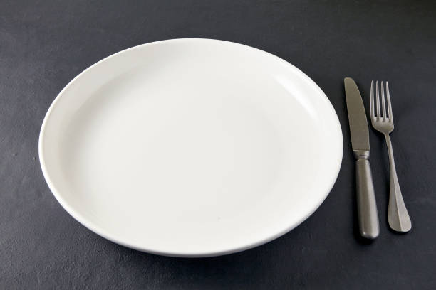 istock Empty white ceramic plate with cutlery on a black stone table. High angle view 1793160257