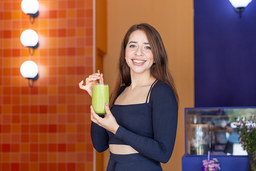Portrait of young woman looking at the camera with a green juice in hand
