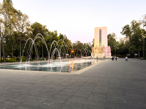La Bombilla public park in the south of Mexico City on a weekend, with families and visitors around an illuminated fountain at sunset
