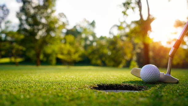 日没時に緑の芝生のゴルフコースでゴルファーによって穴が開けられるゴルフボール。 - golf golf flag sunset flag ストックフォトと画像