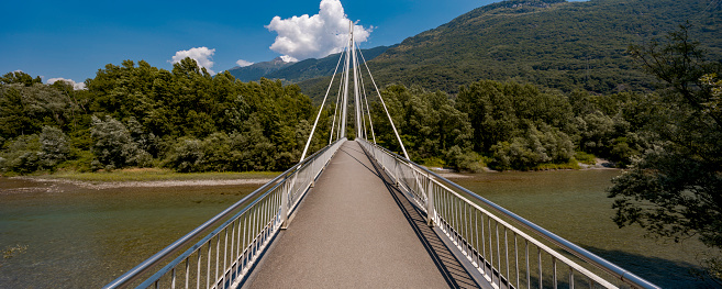 Footbridge in the middle of the forest, beautiful architecture. Below flows the crystalline Ticino river. The object is located in Switzerland, it is a sunny day in the middle of summer. Front view