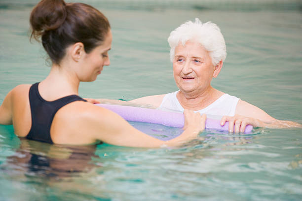 Instructor And Elderly Patient Undergoing Water Therapy Instructor And Elderly Patient Undergoing Water Therapy Holding Inflatable In Hydrotherapy Pool hydrotherapy stock pictures, royalty-free photos & images