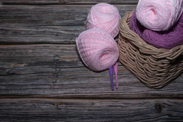 lilac and pink yarn in basket on wooden textured background and two crochet.hook