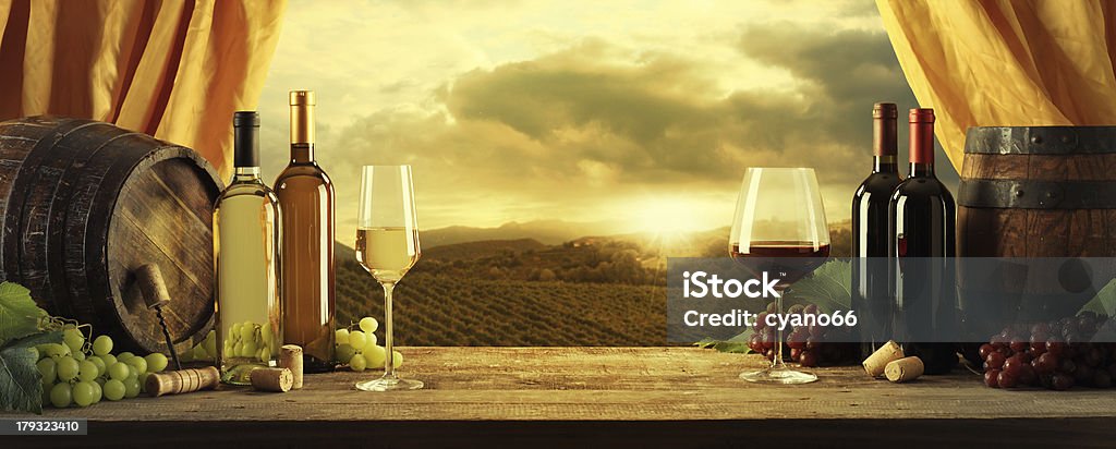 Wine Wine bottles, barrels and vineyard in sunset White Wine Stock Photo