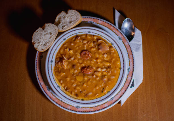 istock TYPICAL SPANISH FABADA IN A PLATE, WITH TWO PIECES OF BREAD AND A SPOON ON A NAPKIN. EVERYTHING IS OVER A WOODEN TABLE 1793235258
