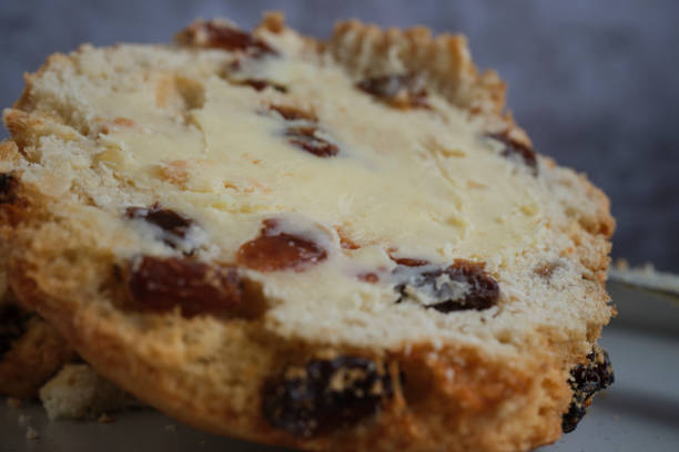 Fresh fruit scone with dishes of cream and jam on a wooden platter in a rustic setting with a mug of coffee