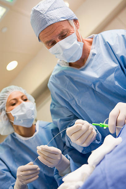 Surgeons Preparing Equipment For Surgery Surgeons Preparing Equipment For Surgery Helping Each Other In Operating Theatre catheter stock pictures, royalty-free photos & images