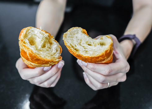 Woman tearing and breaking a croissant in her hand, closed up shot.