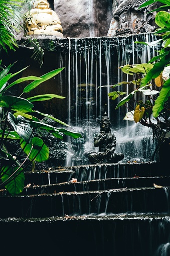A majestic Buddha statue in a peaceful setting in front of a cascading waterfall