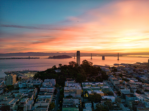 Aerial view of Iconic Coit Tower and the Bay Bridge in  San Francisco at sunrise with  a fiery orange sky.