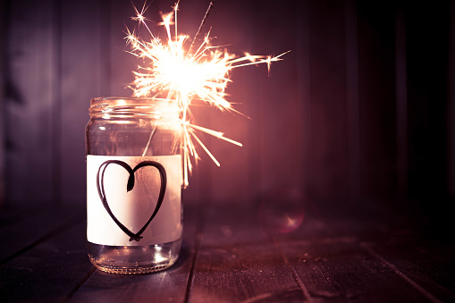 Hope for love, still life with glass jar with heart symbol and burning sparkler. Romantic pink tone. Background with copy space for Valentine.