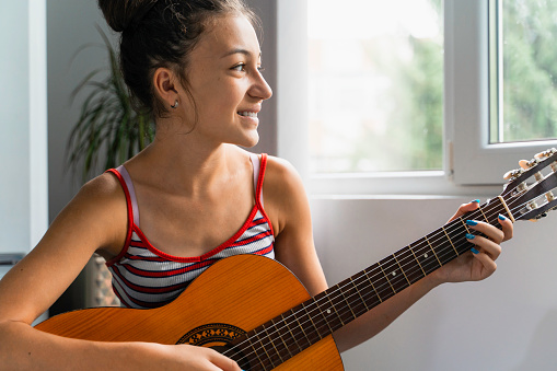 Teenage girl playing guitar at home.