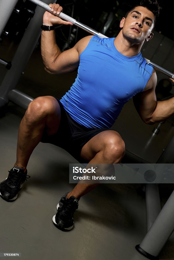 Giovane uomo in T-Shirt blu fare Squat con bilanciere - Foto stock royalty-free di Abbigliamento sportivo