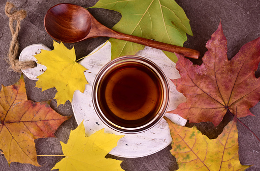 Maple syrup in a bowl on a background of autumn colorful leaves. Flat lei.