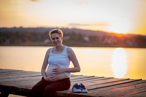 Pregnancy. Pregnant woman. Sunset in the background. Over the water.