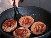 A person flipping over beef patties with a spatula