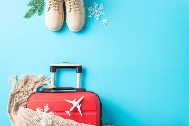 istock New Year's Flight Preparations: top view image of a red suitcase, miniature plane, winter essentials â boots, scarf, garnished with fir twigs and snowflakes against a vibrant blue backdrop 1793330284